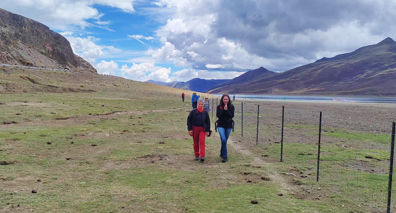 Zwei Reisende wandern durch eine offene Landschaft an einem See in Tibet