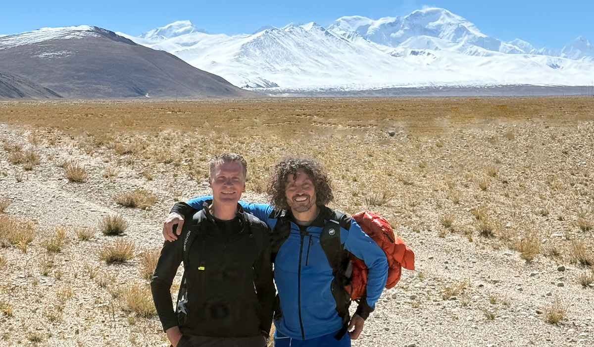 Wanderer beim Trekking auf einem tibetischen Hochplateau vor schneebedeckten Bergen